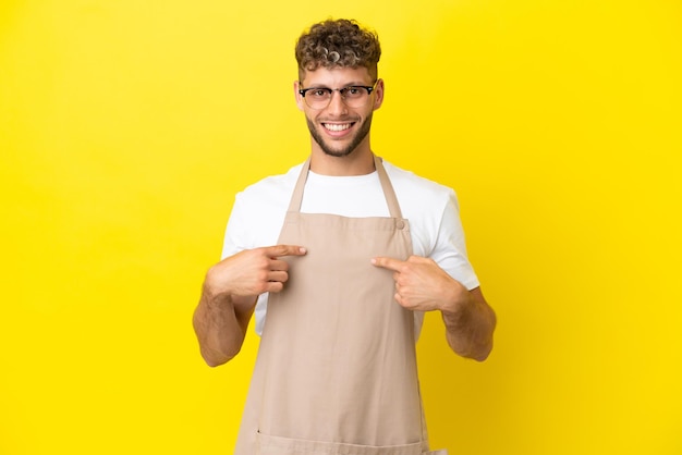 Garçom de restaurante loiro isolado em fundo amarelo com expressão facial de surpresa