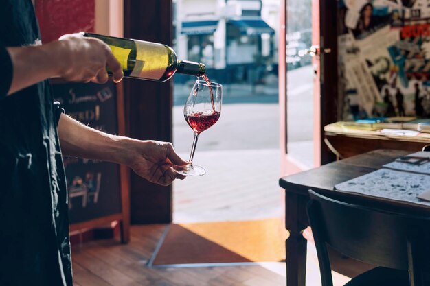 Garçom derramando vinho tinto no copo - vidro na luz de fundo