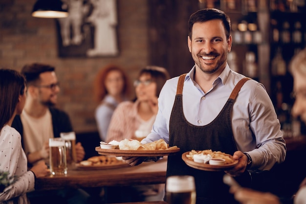 Foto garçom feliz servindo comida e olhando para a câmera em uma taverna