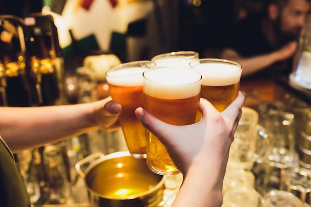Foto garçom segura quatro copos de cerveja nas mãos em um bar ou pub