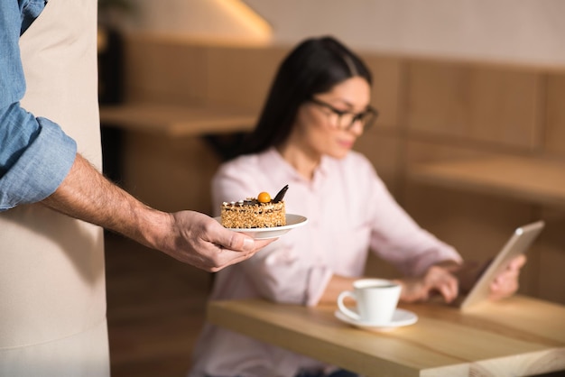 Garçom servindo bolo para empresária usando tablet digital no café foco em primeiro plano