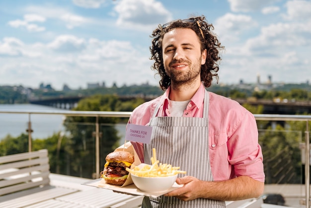 Garçom sorridente. garçom sorridente e simpático se sentindo animado ao trazer pedidos de fast food para seus visitantes