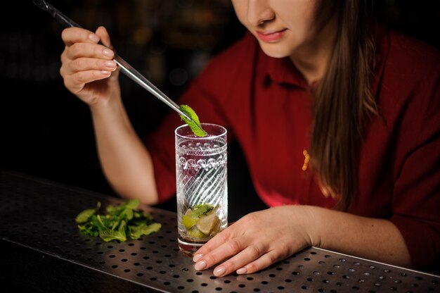 Garçonete bonita em um vestido vermelho prepara um mojito em um copo de cristal