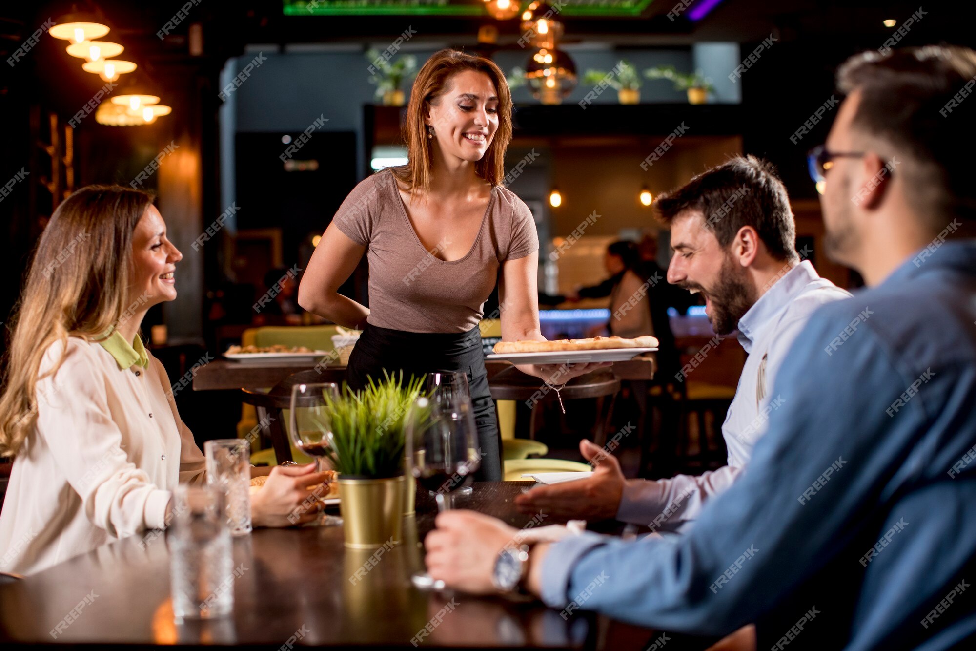 Garçonete bonita servindo grupo de amigas com comida no restaurante