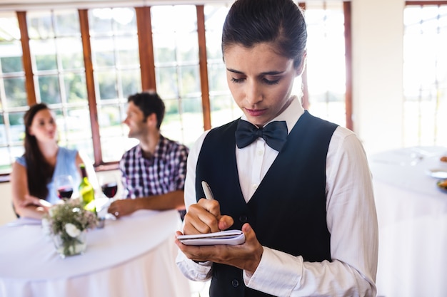 Garçonete, escrevendo a ordem no bloco de notas no restaurante