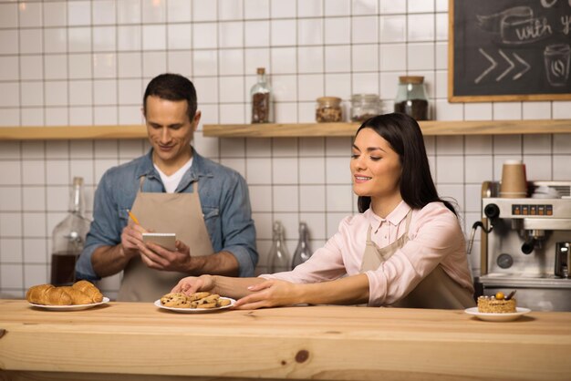 Garçonete pegando biscoitos no prato da mesa enquanto garçom faz anotações