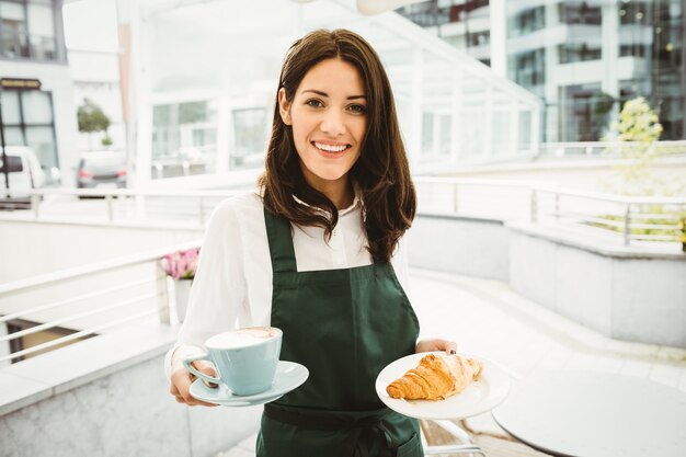 Garçonete, posando com café e croissant no café