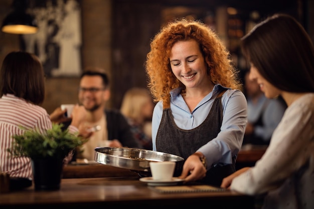 Foto garçonete ruiva feliz servindo uma convidada com uma xícara de café na cafeteria