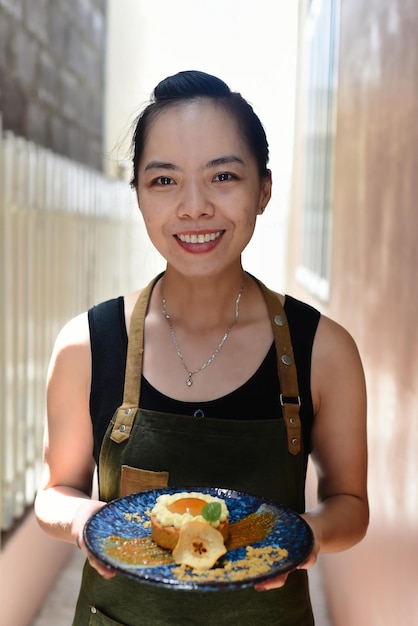 Garçonete vietnamita em avental segurando torta de maçã em um prato azul