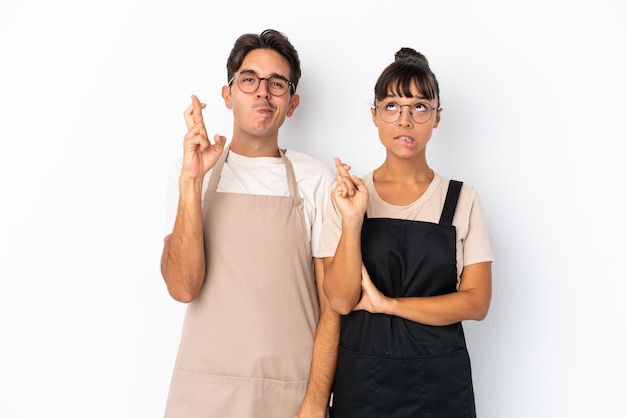 Garçons de restaurante misto isolados no fundo branco com os dedos se cruzando e desejando o melhor