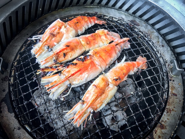 Garen von gegrillten garnelen mit holzkohlegrill durch grillen auf stahlrost. unten ist die holzkohle, die sehr heiß ist.