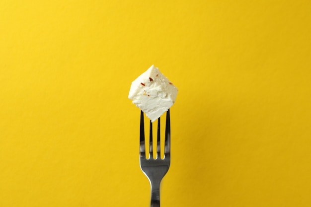 Garfo com pedaço de queijo feta na superfície amarela