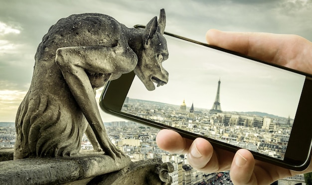 Gárgola en la Catedral de Notre Dame de París mira a la Torre Eiffel en el móvil o teléfono celular París Francia Foto divertida del viejo París y teléfono inteligente