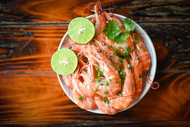 Garnelen auf weißem Bolw und Holzhintergrund Esstisch Essen Frische Garnelen Meeresfrüchte Zitrone Limette mit Kräutern und Gewürzen