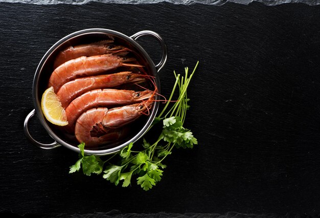 Garnelen Garnelen ungekocht mit Zitrone und Petersilie auf schwarzem Schieferhintergrund, Ansicht von oben. Meeresfrüchte