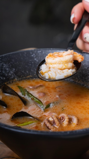 Garnelen und Reis auf Löffel in der Hand der Frau auf dem Hintergrund von Tom-Yum-Suppe