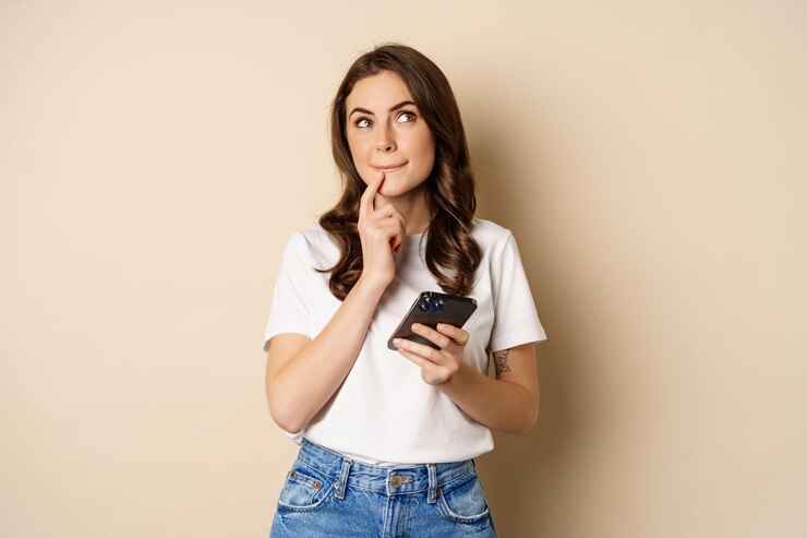 Foto garota acha que segura telefone celular procura suportes pensativos sobre fundo bege