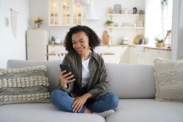 Garota adolescente afro-americana usa aplicativos de telefone modernos conversando na rede social fazendo compras on-line em casa