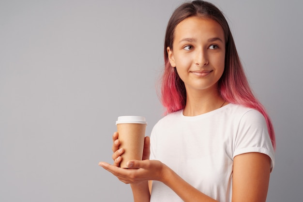 Garota adolescente agradável, segurando uma xícara de café sobre um fundo cinza