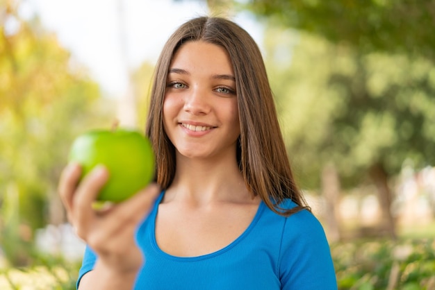 Garota adolescente ao ar livre segurando uma maçã com expressão feliz