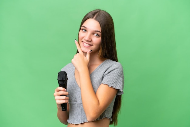 Garota adolescente cantora pegando um microfone sobre fundo isolado feliz e sorridente