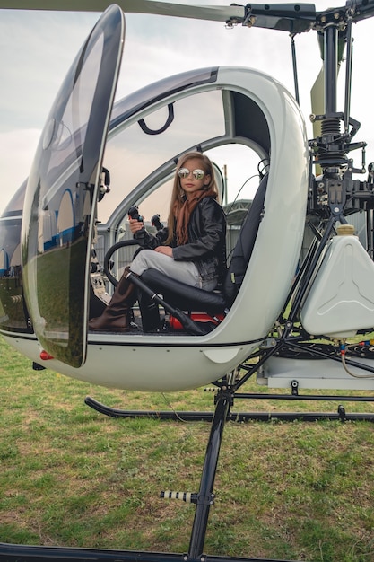 Garota adolescente com óculos escuros espelhados sentada no assento do piloto em um helicóptero