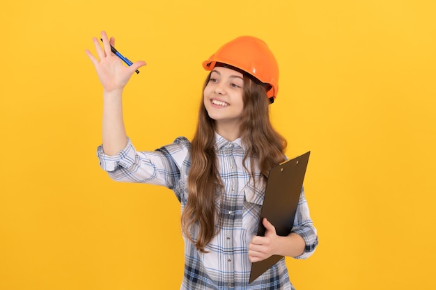 Garota adolescente de carreira futura no capacete fazendo anotações, criança, escrevendo na pasta, construção e construção, trabalhador infantil feliz, use capacete de segurança, segure a área de transferência, gesticulando infância, feliz dia do trabalho