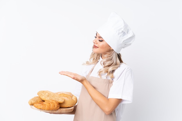 Garota adolescente em uniforme de chef. Padeiro feminino segurando uma mesa com vários pães sobre branco isolado, estendendo as mãos para o lado para convidar para vir