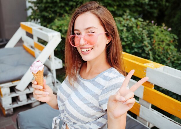 Garota adolescente engraçada em óculos de sol hipster legal comendo casquinha de sorvete. Comida de verão