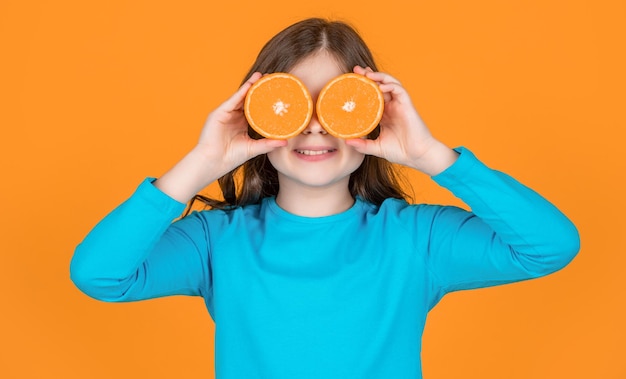 Garota adolescente engraçada segura fruta laranja em fundo amarelo