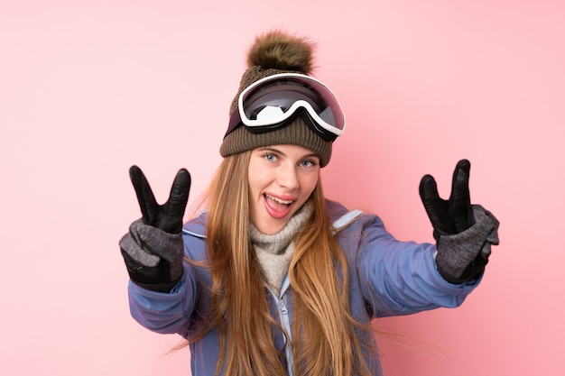 Garota adolescente esquiador com fundo de óculos de snowboard sorrindo e mostrando sinal de vitória