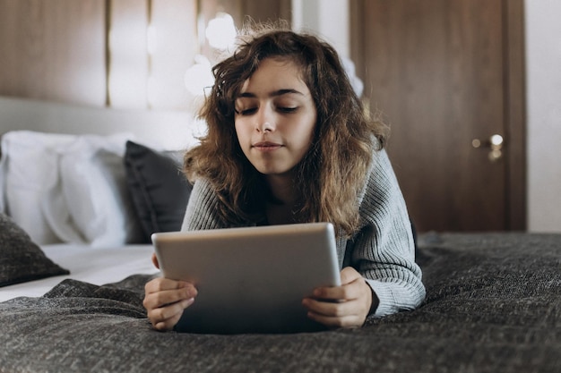 Garota adolescente feliz assistindo vídeo no tablet bate-papo online com amigos garota deitada na cama