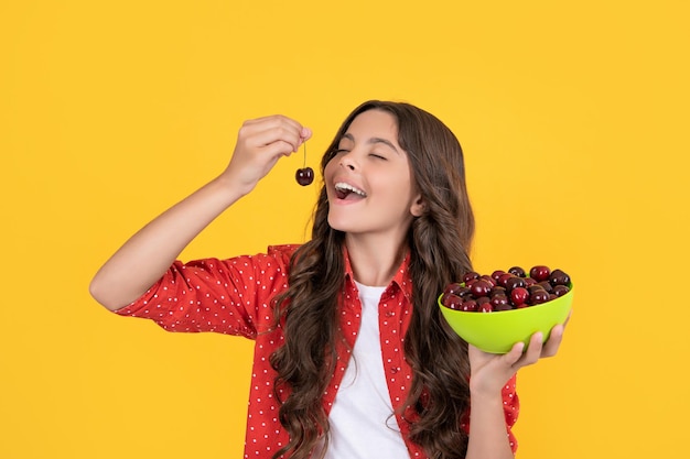 Foto garota adolescente feliz come tigela de cereja em fundo amarelo