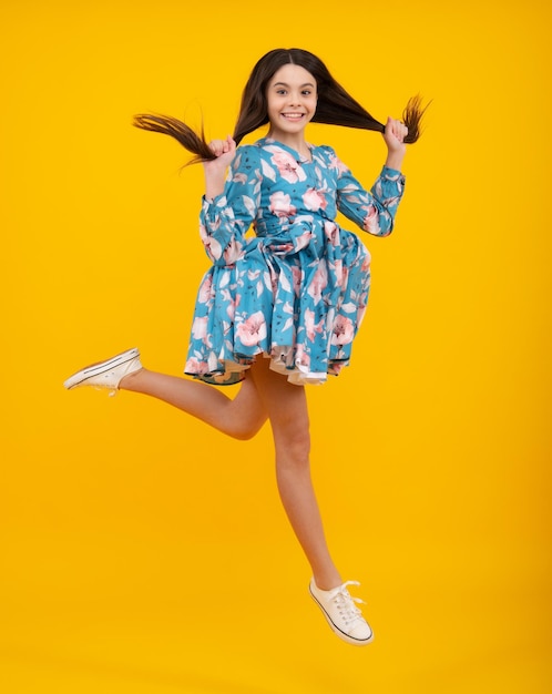 Garota adolescente feliz de comprimento total 12 13 14 anos pulando isolado no estúdio de fundo amarelo Salto engraçado Criança no vestido de movimento de verão