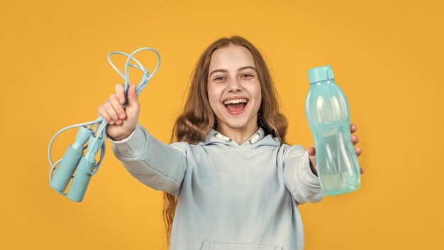 Garota adolescente feliz e sorridente segura equipamento esportivo ou fitness de pular corda e refresco de garrafa de água