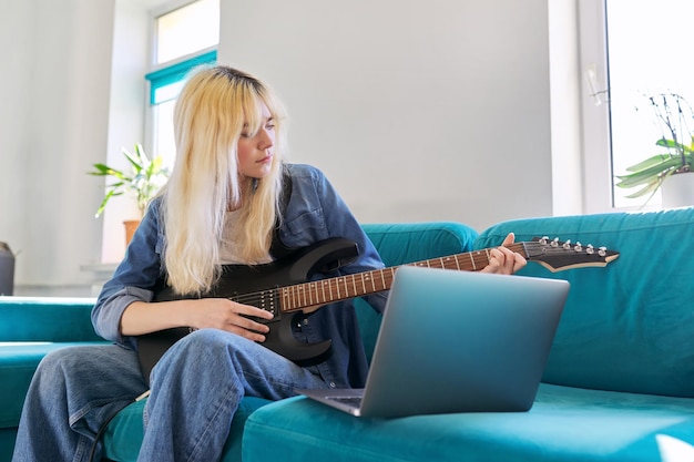 Garota adolescente hipster tocando guitarra elétrica olhando para o monitor do laptop