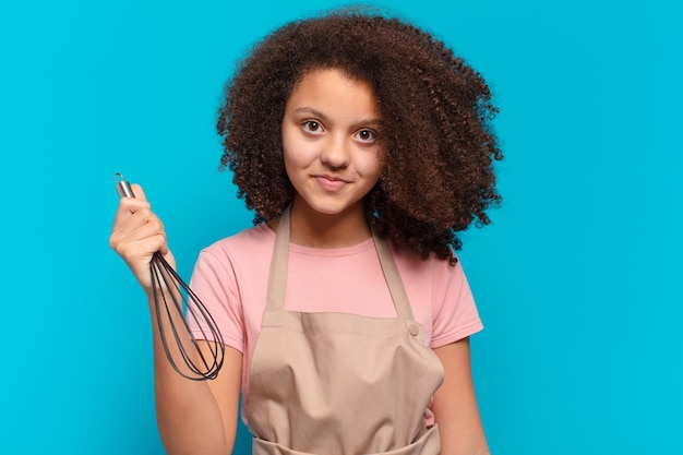 Garota adolescente muito afro cozinhando com um avental e um conceito de padeiro misturador