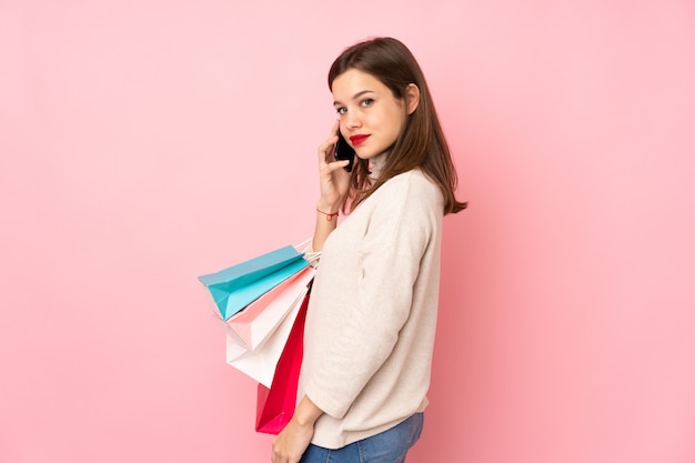 Garota adolescente na parede rosa segurando sacolas de compras e ligar para um amigo com seu telefone celular