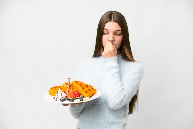 Garota adolescente segurando waffles sobre fundo branco isolado com dúvidas