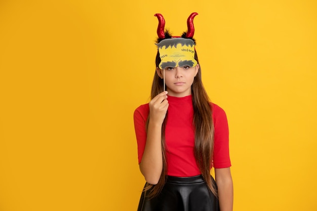 Garota adolescente séria usando chifres de imp segurando acessório de festa em fundo amarelo dia das bruxas