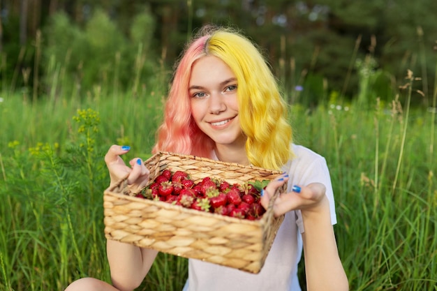 Garota adolescente sorridente com morangos na cesta, fundo da natureza do jardim, comida vitamínica orgânica natural saudável, temporada de morango