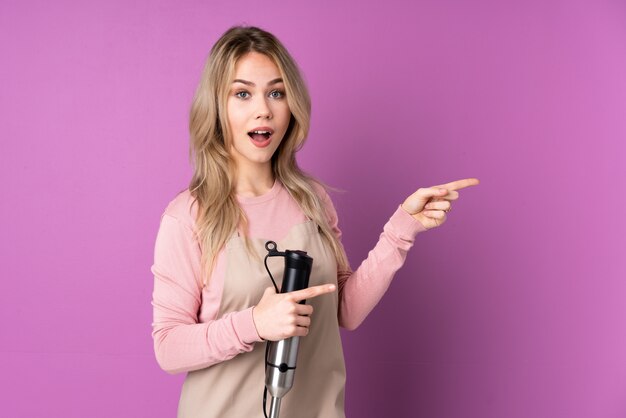 Foto garota adolescente usando o liquidificador na parede roxa surpreendeu e apontando o lado