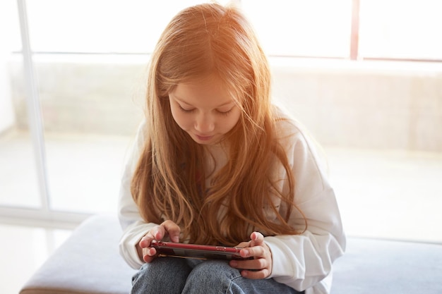 Garota adolescente verificando as mídias sociais usando smartphone em casa garota relaxando jogando jogos para celular pedindo...