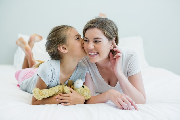 Garota adorável beijando a mãe deitada em uma cama