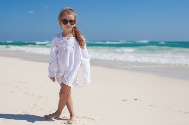 Garota adorável criança vestida de branco andando na praia exótica