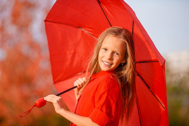 Garota adorável feliz com guarda-chuva vermelho no outono