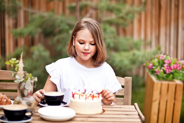 Garota adorável feliz comendo bolo de aniversário no terraço do café. criança de 10 anos comemora aniversário.