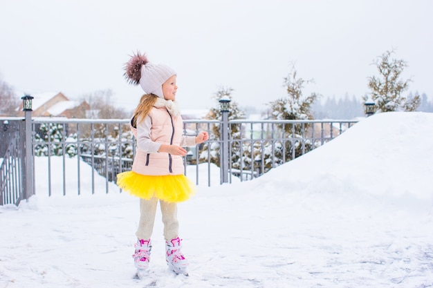 Garota adorável patinar na pista de gelo ao ar livre em dia de neve do inverno