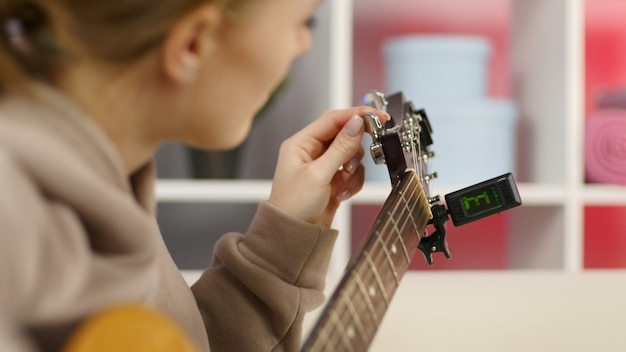 Garota afina uma guitarra usando um afinador