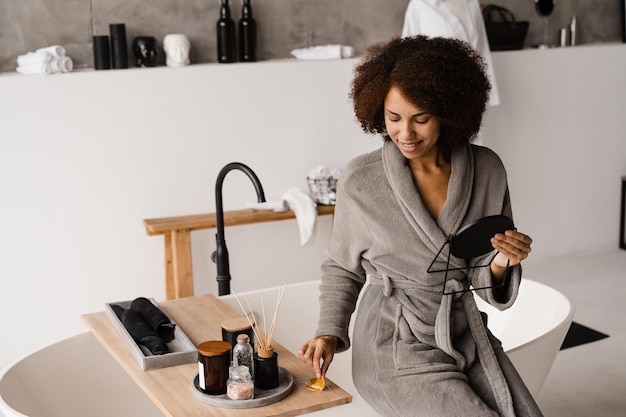 Garota africana sorridente com tapa-olhos dourados em roupão de banho no banheiro Procedimento cosmético para suavizar rugas remove inchaço ou bolsas sob os olhos